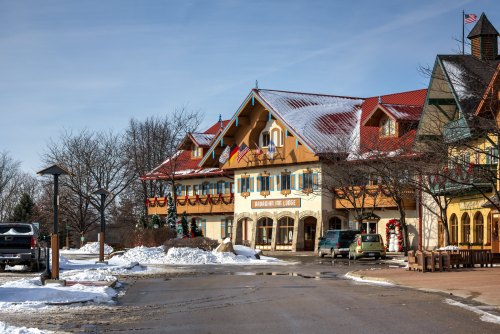 A charming lodge with festive decorations, surrounded by snow and trees, under a clear blue sky.
