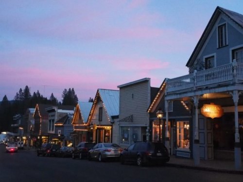 A charming street lined with historic buildings, adorned with lights, under a pastel pink sky at dusk.