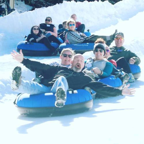 A group of people enjoying snow tubing, laughing and having fun on a snowy slope.