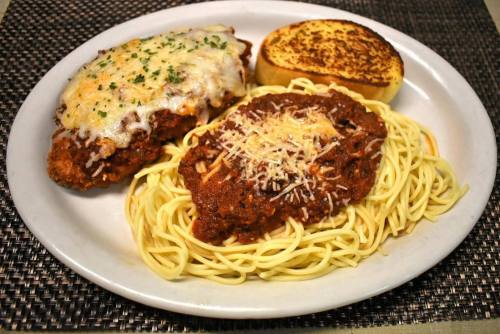 A plate of spaghetti with marinara sauce, topped with cheese, alongside a breaded chicken breast and garlic bread.