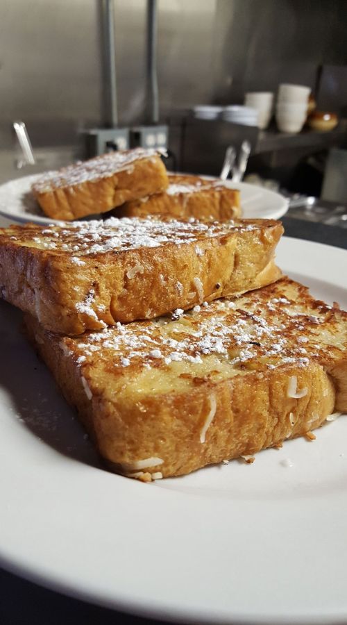 Three slices of golden-brown French toast dusted with powdered sugar, served on a white plate.