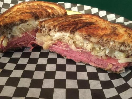 A close-up of a toasted sandwich filled with layers of corned beef and sauerkraut, served on a checkered plate.