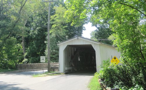 A white covered bridge surrounded by greenery, with road signs indicating to keep right and a height limit.