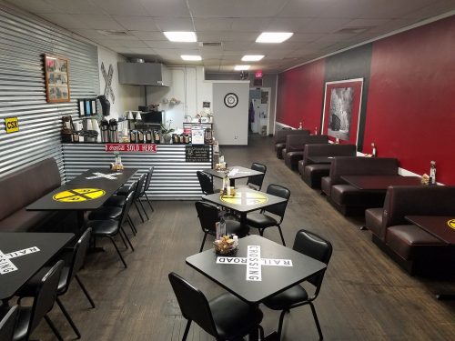 A cozy diner with black tables, booths, and a retro decor featuring railroad signs and a striped wall.