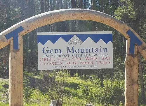 Sign for Gem Mountain, stating hours and days open for sapphire gemstone mining in Philipsburg.