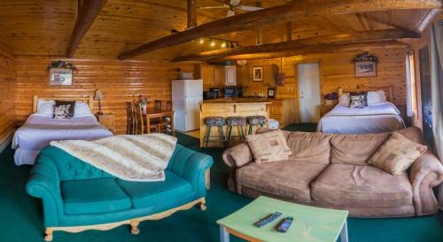 Cozy cabin interior with two beds, a sofa, kitchenette, and wooden beams, creating a warm, inviting atmosphere.
