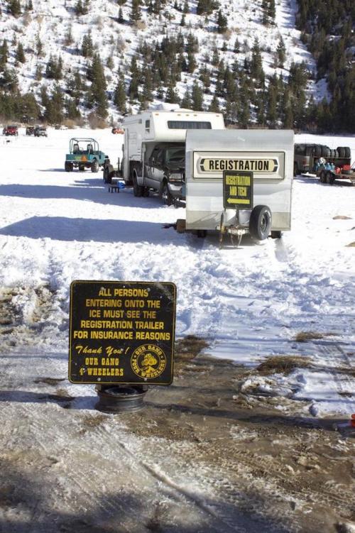A snowy scene with a registration trailer and a sign warning about insurance for ice entry, surrounded by vehicles.