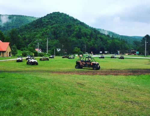 A grassy field with several ATVs parked, surrounded by green hills and a cloudy sky.