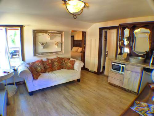 Cozy room featuring a white couch with floral pillows, a mirror, kitchenette, and a bed visible in the background.