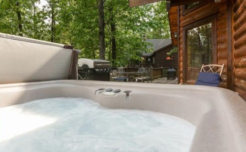 A hot tub with bubbling water, surrounded by trees and a wooden cabin in the background.