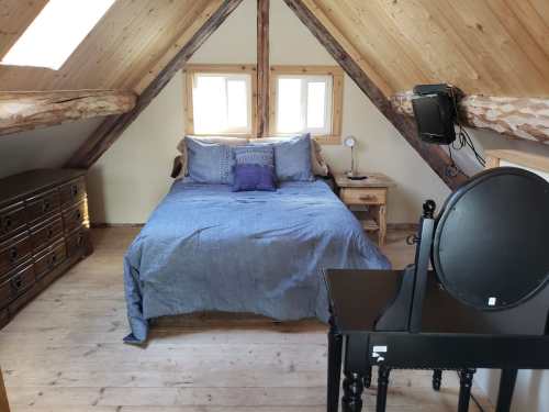 Cozy attic bedroom with a wooden bed, nightstand, dresser, and a mirror, featuring sloped ceilings and natural light.