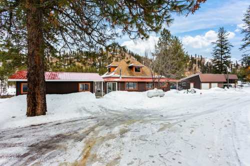 A snow-covered landscape featuring a rustic house with a red roof, surrounded by trees and mountains in the background.