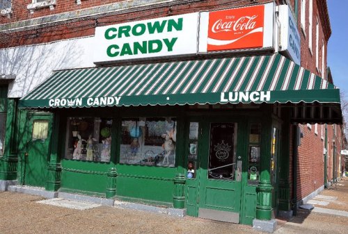 A vintage candy shop with a green awning, striped canopy, and a Coca-Cola sign above the entrance.