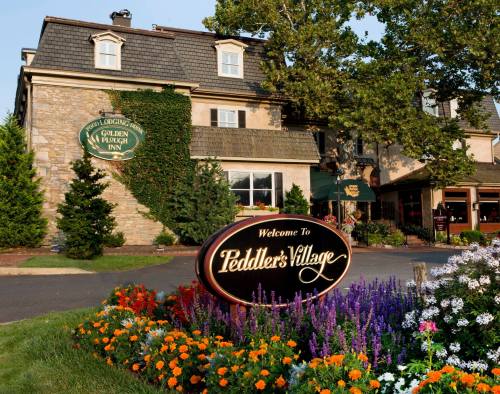 A charming inn with stone exterior and colorful flower beds, featuring a sign that reads "Welcome to Peddler's Village."