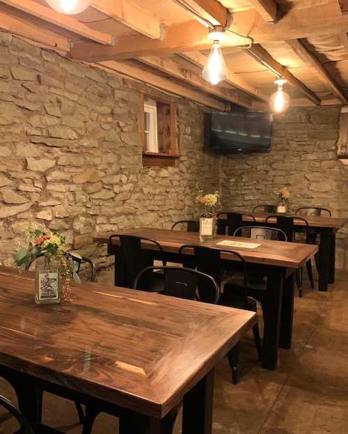 Cozy dining area with wooden tables, stone walls, and warm lighting, featuring small flower arrangements on each table.
