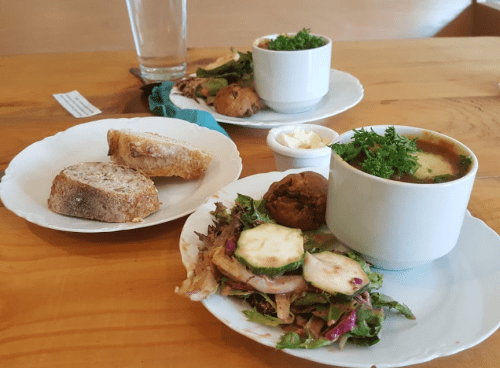 A plate with salad, soup, and a small dessert, alongside a side of bread on a wooden table.