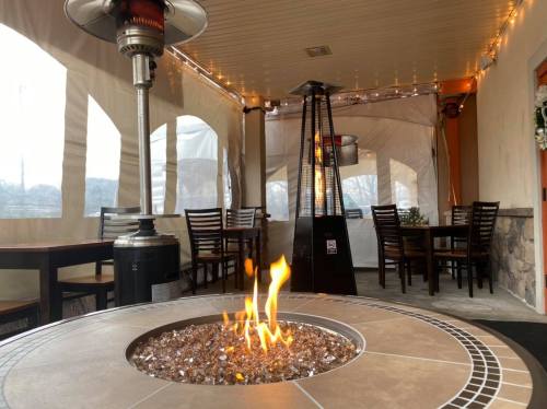 Cozy outdoor dining area with a fire pit, patio heaters, and string lights, enclosed by clear plastic walls.