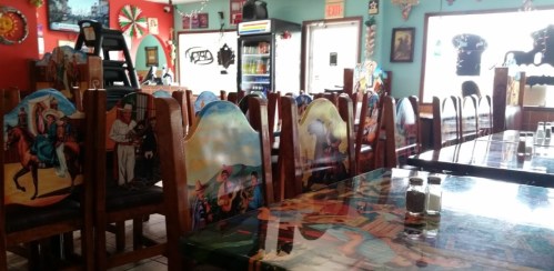 Colorful restaurant interior with decorated chairs and tables, featuring vibrant artwork and a cozy atmosphere.