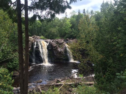 A serene waterfall cascades over rocky cliffs, surrounded by lush green trees and a calm river below.
