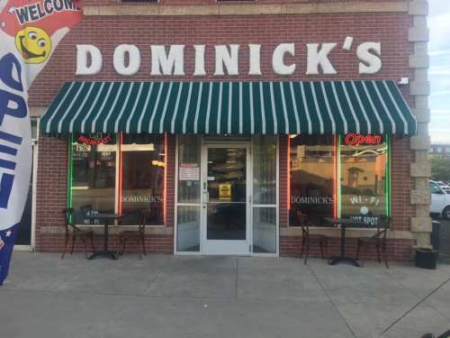 Exterior of Dominick's restaurant with a green and white striped awning, open sign, and outdoor seating.