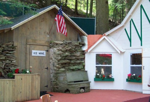 A rustic building with an American flag, featuring a stone facade and colorful flower boxes, set in a wooded area.