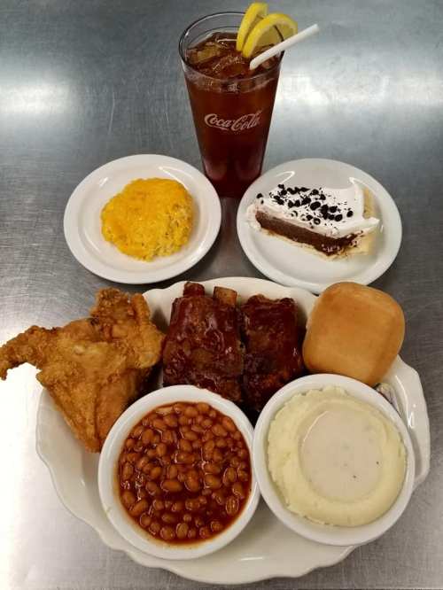 A hearty meal featuring fried chicken, ribs, baked beans, mashed potatoes, cornbread, and dessert, with iced tea.
