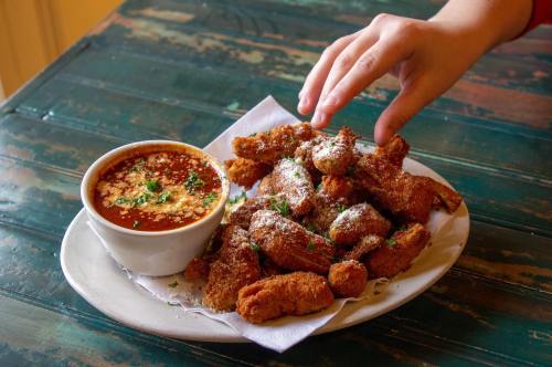 A plate of crispy fried food with a bowl of dipping sauce, garnished with herbs, and a hand reaching for a piece.