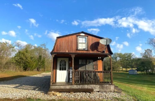 A small wooden cabin with a satellite dish, surrounded by greenery and blue skies.