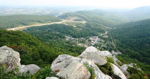 A panoramic view from a rocky overlook, showcasing lush green mountains and a small town below.
