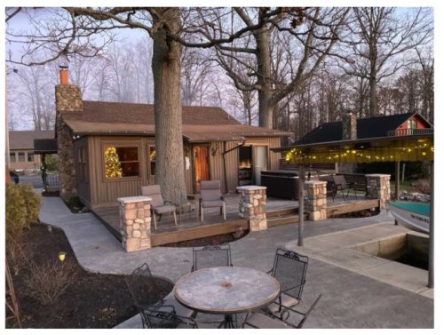 A cozy cabin with a stone exterior, surrounded by trees, featuring a patio and outdoor seating area.