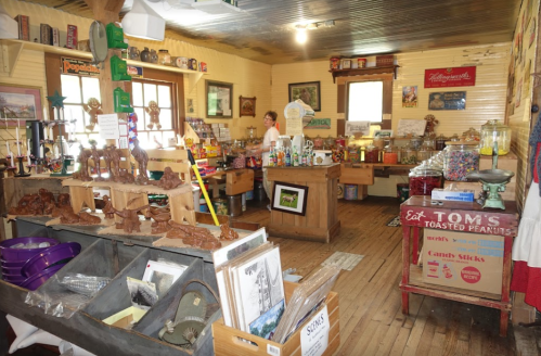A cozy vintage store filled with various goods, wooden carvings, and colorful candies, with a person organizing items.