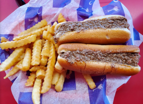 Two hot dog buns filled with meat, served with a side of crinkle-cut fries on a patterned paper.