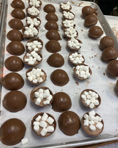 A tray of chocolate cups filled with mini marshmallows, arranged in neat rows on parchment paper.