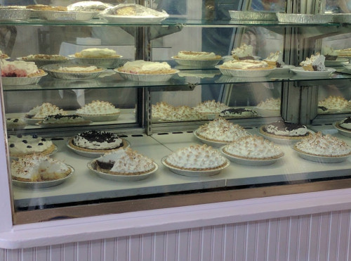 A display case filled with various pies, featuring meringue toppings and different crusts, in a bakery setting.
