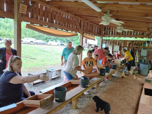 A group of people sifting through materials at a covered outdoor area, with tools and buckets on a long table.