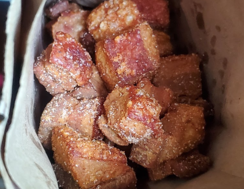 Crispy, golden-brown pork belly pieces in a brown paper bag, lightly seasoned and ready to eat.