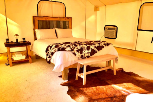Cozy glamping tent interior featuring a bed, wooden bench, and decorative cowhide rug. Warm, inviting atmosphere.