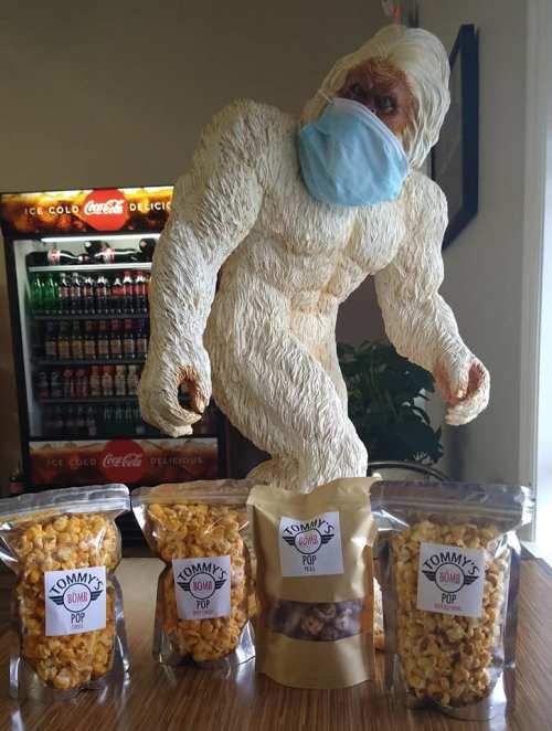 A yeti statue wearing a mask stands near bags of popcorn labeled "Tommy's Bomb Pop." A soda machine is in the background.