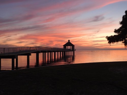 A serene pier extends into calm waters, framed by a vibrant sunset with pink and orange hues.