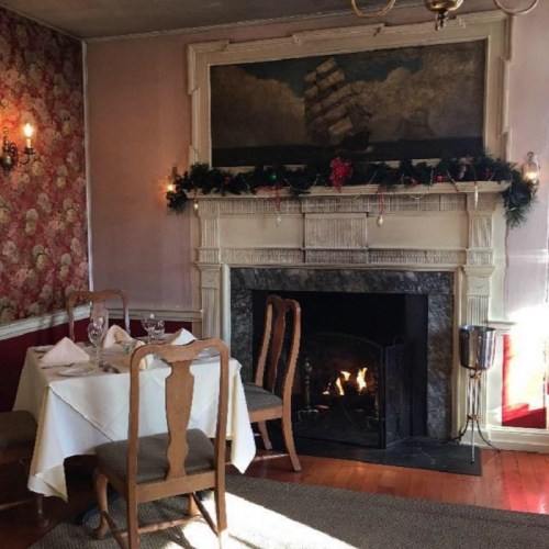 Cozy restaurant interior with a fireplace, ship painting, and festive decorations on the mantel.