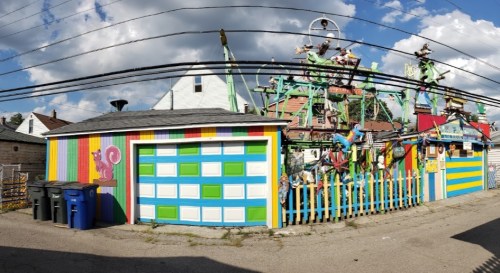 Colorful alley scene featuring a vibrant mural on a garage and whimsical decorations on a nearby fence.