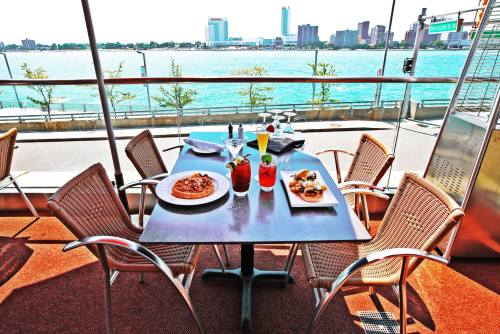A table set with drinks and food overlooks a waterfront view of a city skyline on a sunny day.
