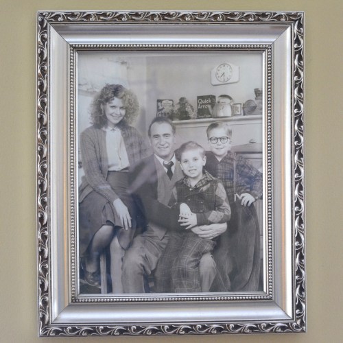 A black-and-white family portrait in a decorative frame, featuring two adults and two children smiling together.