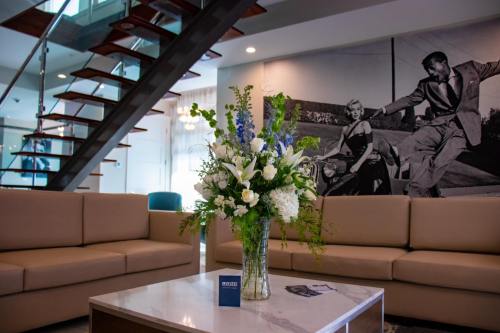 A modern living space with a staircase, floral arrangement on a table, and a vintage black-and-white mural in the background.