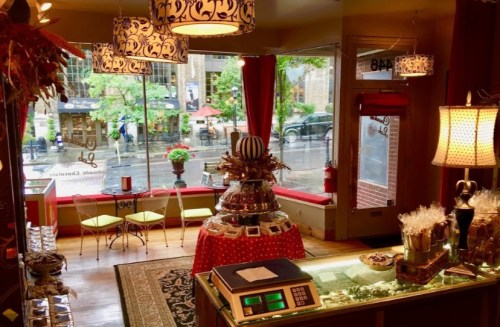 Cozy chocolate shop interior with a display of treats, bright decor, and a view of a rainy street outside.