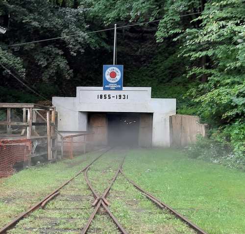 Entrance to a historic tunnel with a sign reading "1855-1931," surrounded by greenery and railway tracks.
