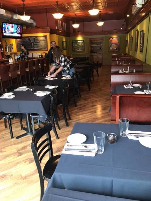 A restaurant interior with black tablecloths, empty tables, and a staff member setting a table.
