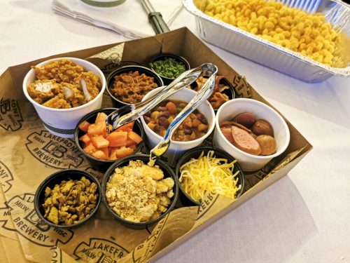 A tray with various small bowls of toppings, including meats, beans, cheese, and vegetables, alongside a container of snacks.