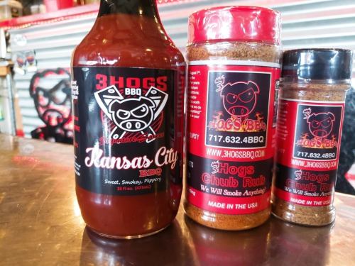 Three BBQ products: a bottle of Kansas City BBQ sauce and two jars of spice rubs, all branded with a pig logo.