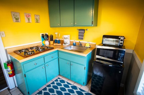Bright kitchen with yellow walls, teal cabinets, a sink, stove, microwave, and a small black fridge. Cozy and colorful decor.